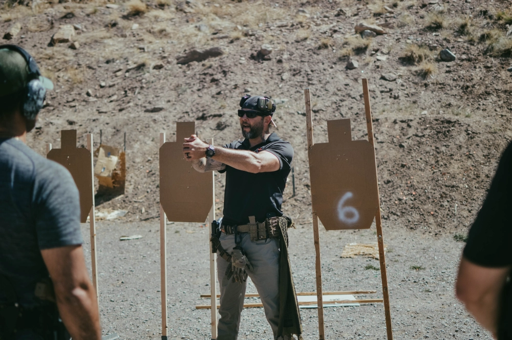 Instructor demonstrating Tactical Carbine Training techniques to a group at an outdoor shooting range, with targets in the background.